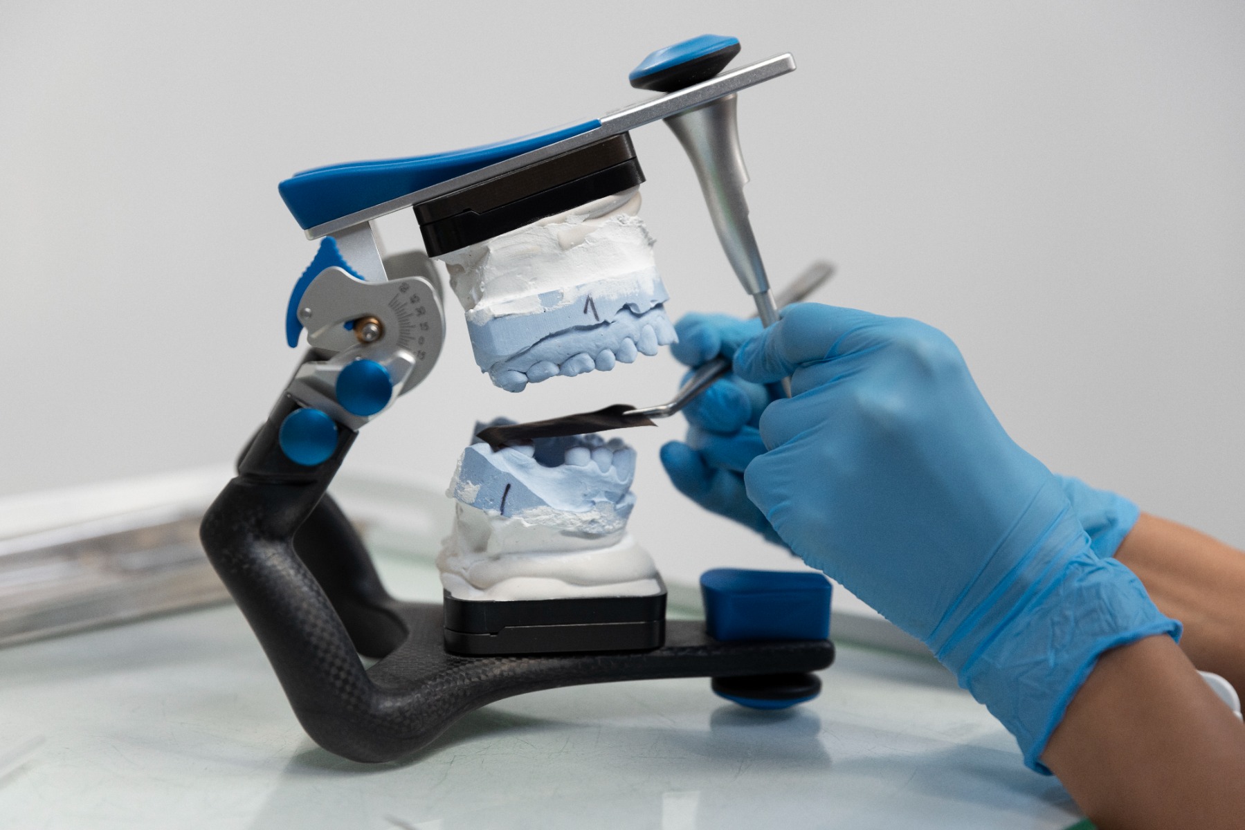 Les mains d'un dentiste manipulant un articulateur dentaire.